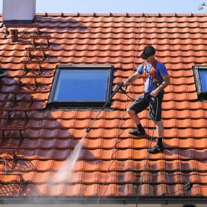 Man pressure washing a red tile roof.